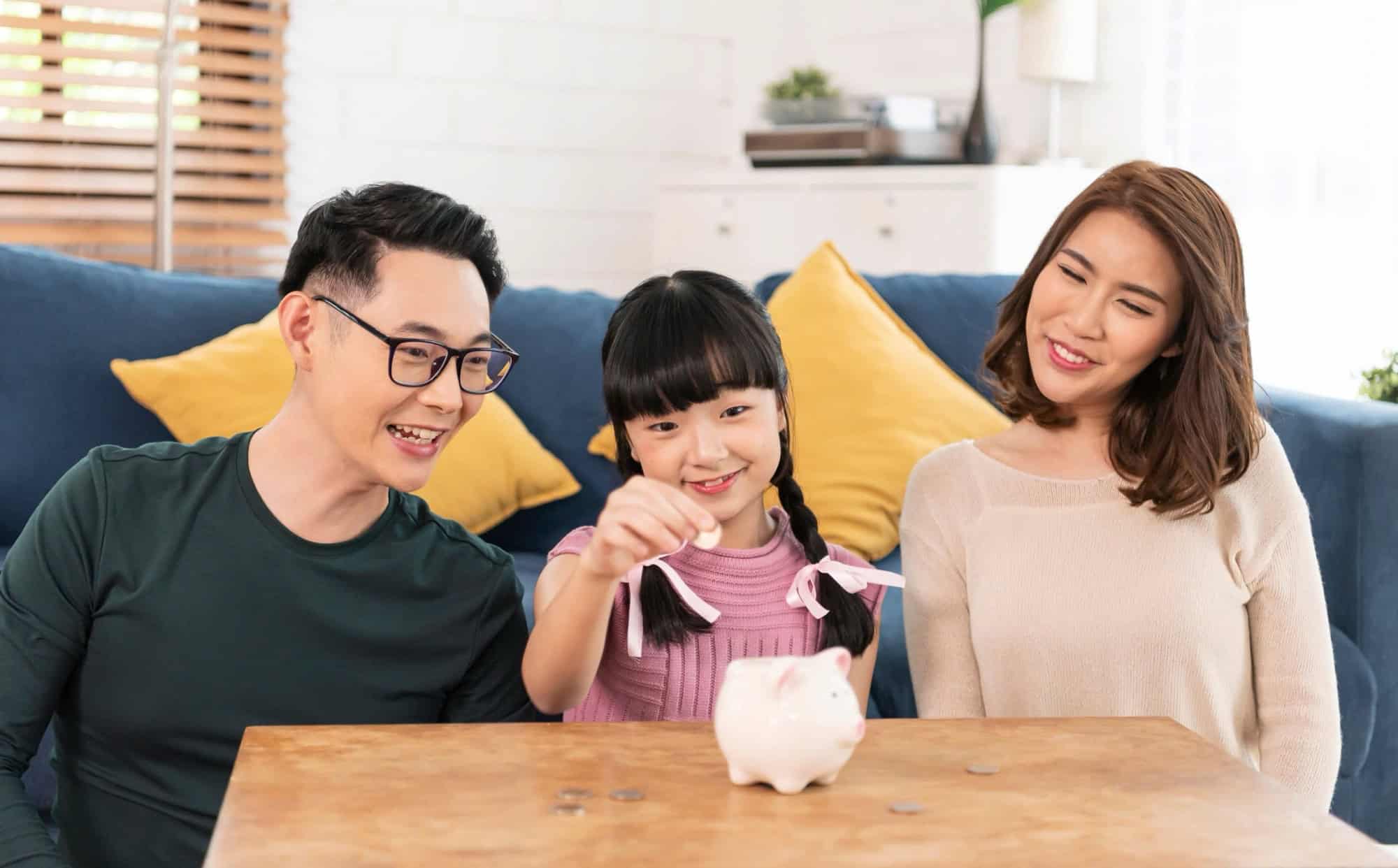 Gia đình hạnh phúc, bố mẹ và con gái đang vui vẻ bỏ đồng xu vào ống heo để tiết kiệm tiền.